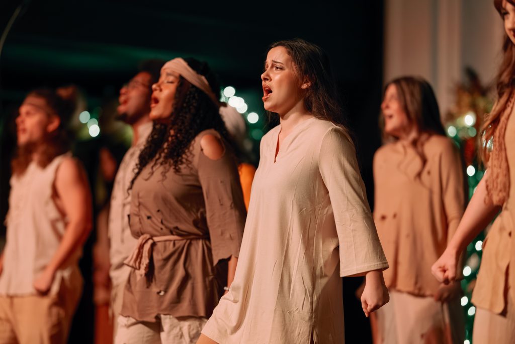 Chorus members singing on stage in biblical-times attire.