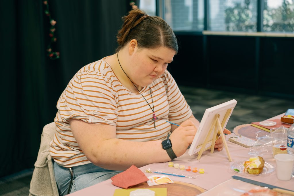 Student paints a canvas at table.