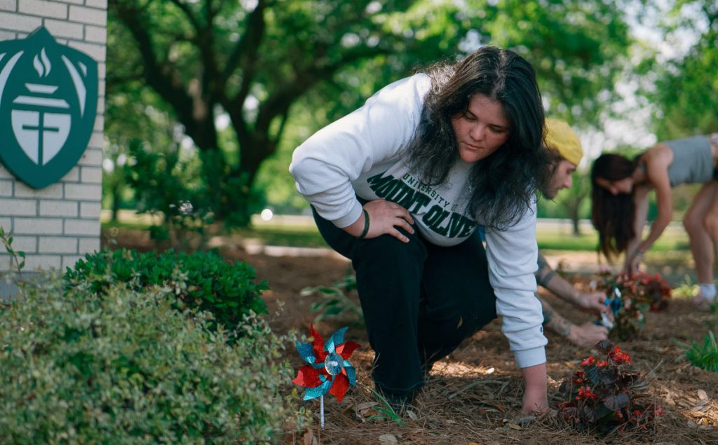 Girl placing pinwheel in garden bed.