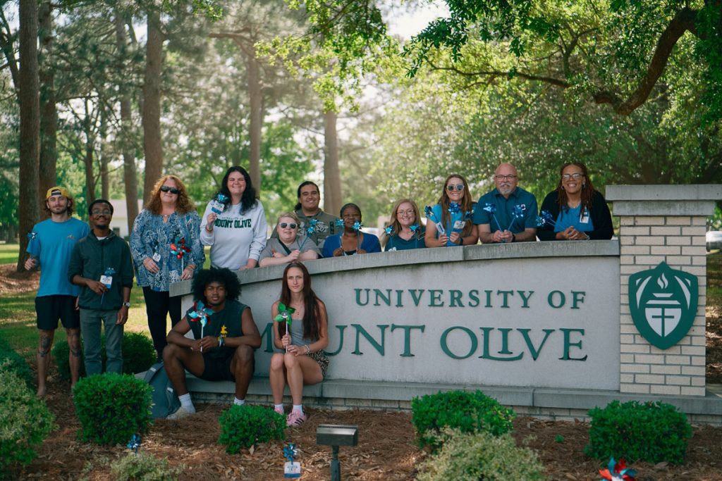 Group of students standing in front of the University of Mount Olive sign.