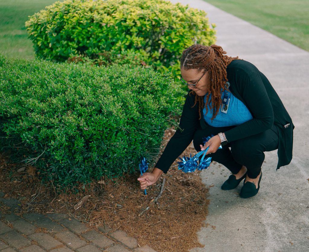 Woman placing a blue pinwheel in garden bed.