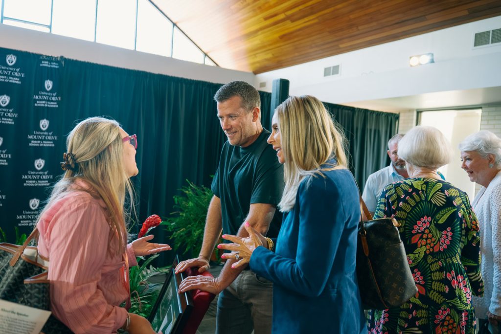 Two people greeting a student at a university event.