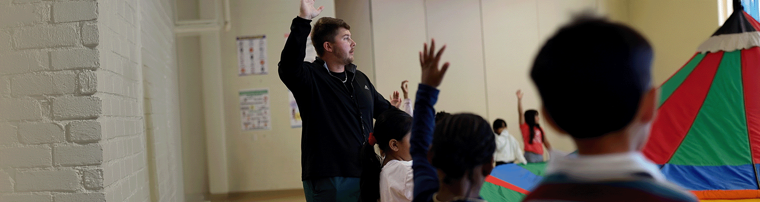 PE_Web Banner Header@0.5x Health and PE Teacher instructing students on how to play the parachute game in class.